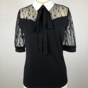 May include: Black blouse with a white collar and a black bow tie. The blouse has sheer star-patterned sleeves.