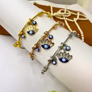 May include: Three gold, rose gold, and silver bracelets with blue evil eye charms. Each bracelet has a cable chain design and multiple charms with blue evil eyes and clear rhinestones.