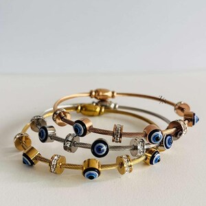 May include: Three gold, silver, and rose gold bracelets with a cable chain design and blue evil eye charms. Each bracelet has a row of clear cubic zirconia stones.