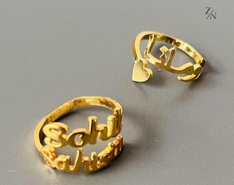 May include: Two gold rings with names written on them. The ring on the left says "Schuh" and "Sahlsten". The ring on the right has Arabic script.