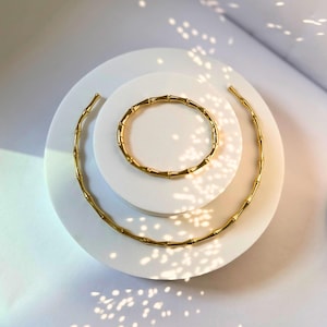 Op de afbeelding: Een set van twee gouden armbanden in bamboestijl. De grotere armband is een ketting en de kleinere armband is een armband.