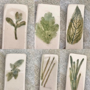 May include: Six rectangular ceramic tiles with different pressed botanical designs. The tiles feature a variety of leaves and flowers, including a single leaf, a cluster of leaves, a single flower, and a group of stems.