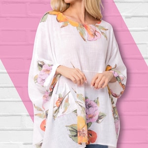 Puede incluir: Túnica blanca con estampado floral, cuello redondo y mangas anchas. La túnica presenta un diseño floral colorido en tonos rosa, naranja y verde. La parte superior se combina con unos vaqueros azules. El logotipo de La Capa Moda Italiana es visible en la esquina superior izquierda.