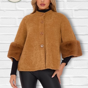 Peut inclure: Une veste texturée marron clair avec un col rond, quatre boutons sur le devant et des manches larges à revers en fausse fourrure marron. Le vêtement est porté sur un haut noir à manches longues et un pantalon noir. Un logo circulaire avec des citrons et le texte LaCapa MODA ITALIANA est visible.