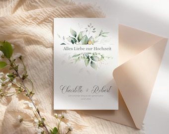 May include: A white card with green watercolor floral designs and the text "Alles Liebe zur Hochzeit" and "Charlotte & Robert" with the date "22.07.2022" and the text "Der schönste Weg ist der gemeinsame"  The card is sitting on a light pink envelope and a beige fabric background.