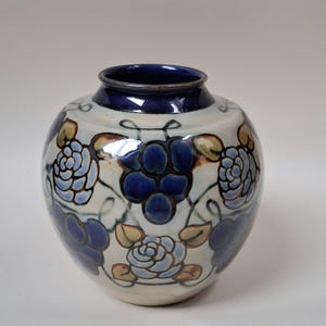 May include: A ceramic vase with a round body and a dark blue rim. The vase is decorated with blue floral patterns and accents on a cream-colored background. The vase is approximately 7 inches tall.