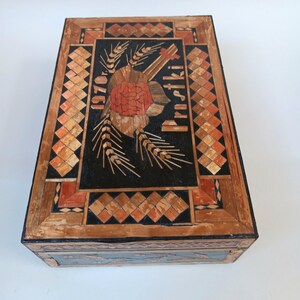 May include: A wooden box with a black background and a straw inlay design. The design features a red rose, wheat stalks, and the text "1970" and "Proszki".