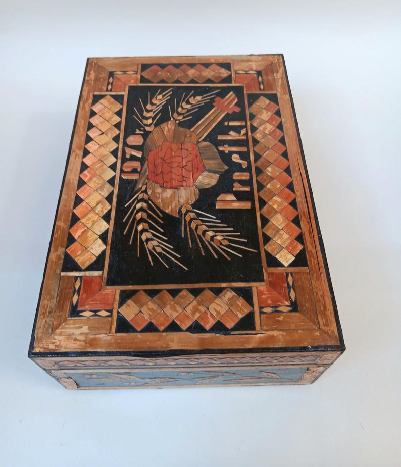 May include: A wooden box with a black background and a straw inlay design. The design features a red rose, wheat stalks, and the text "1970" and "Proszki".