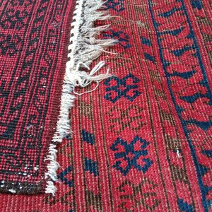 May include: Close-up of a section of a red and black patterned rug. The rug features a geometric design with a fringe edge. The colors are deep red, black, and a touch of blue.