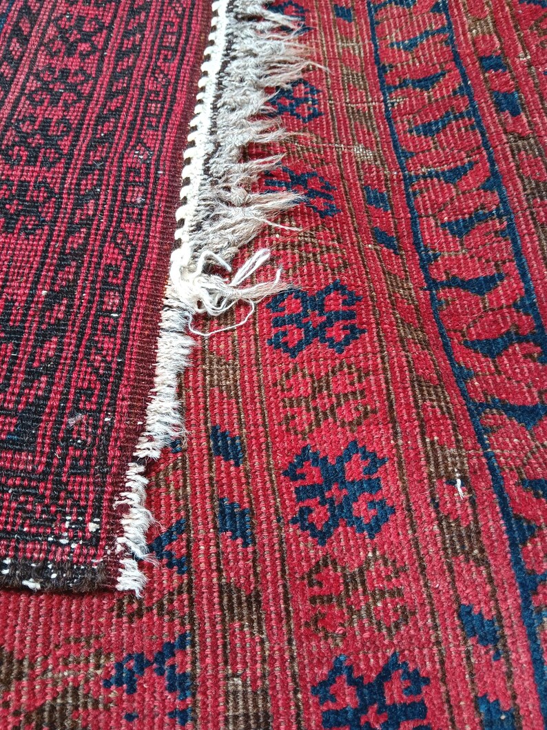 May include: Close-up of a section of a red and black patterned rug. The rug features a geometric design with a fringe edge. The colors are deep red, black, and a touch of blue.
