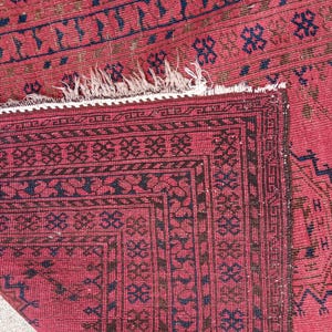 May include: Close-up of a red and black patterned rug. The rug features a detailed geometric design with dark blue and brown accents. The edges have a decorative border and a white fringe.