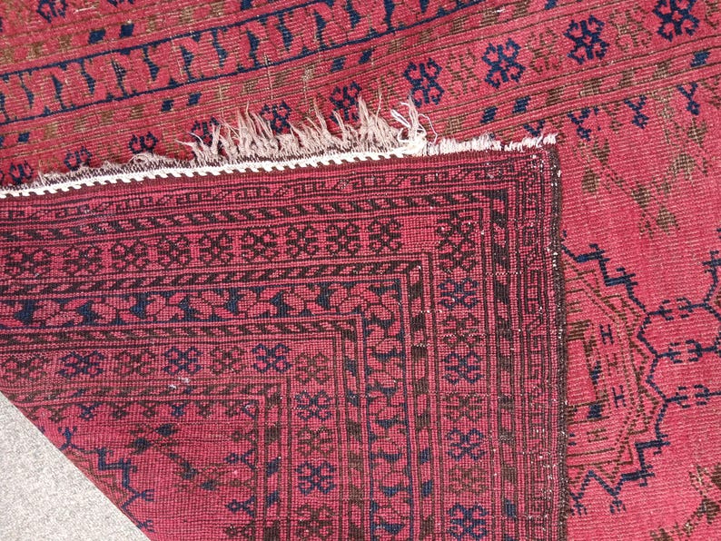 May include: Close-up of a red and black patterned rug. The rug features a detailed geometric design with dark blue and brown accents. The edges have a decorative border and a white fringe.