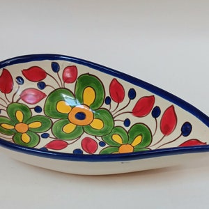 May include: A white ceramic serving dish with a blue rim and a floral design. The flowers are painted in shades of red, yellow, green, and blue.