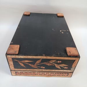 May include: A black wooden box with a floral design inlaid in wood. The box has a hinged lid and four small wooden feet.