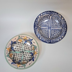 May include: Two decorative ceramic bowls with intricate patterns. One bowl features a blue and white design, while the other has a colourful floral motif with blue, yellow, and green accents. Both bowls are round and sit on a white surface.