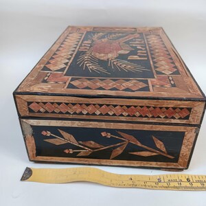 May include: A vintage wooden box with intricate straw marquetry designs. The top features a floral motif with the words "Old English" and the side features a floral design.