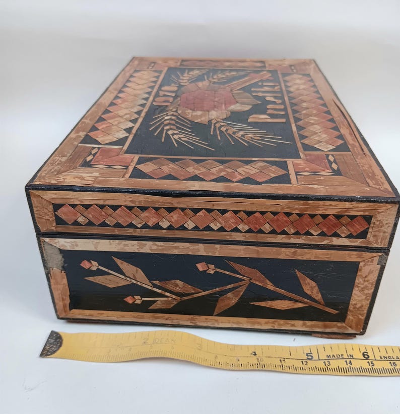 May include: A vintage wooden box with intricate straw marquetry designs. The top features a floral motif with the words "Old English" and the side features a floral design.