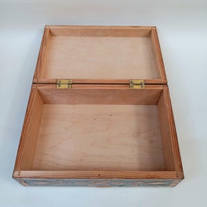 May include: A wooden box with a hinged lid and brass hinges. The box is decorated with intricate carvings on the exterior. The interior of the box is lined with wood.