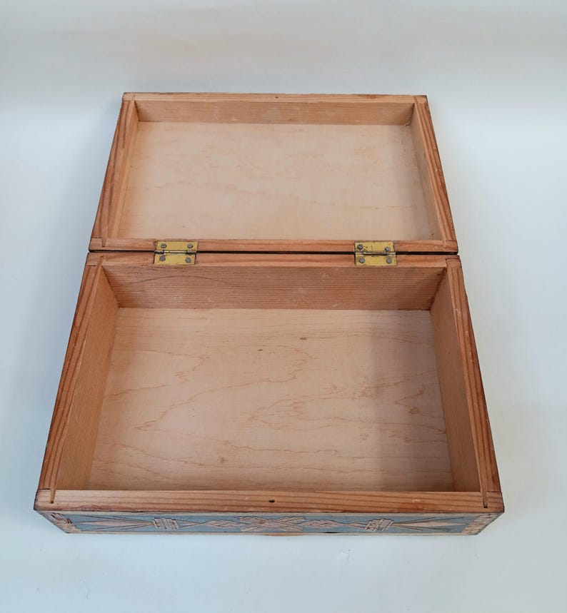 May include: A wooden box with a hinged lid and brass hinges. The box is decorated with intricate carvings on the exterior. The interior of the box is lined with wood.