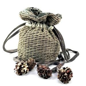 Peut inclure: Un petit sac à cordon de couleur beige et marron avec une doublure en tissu à motifs. Le sac a une longue sangle marron avec des glands.