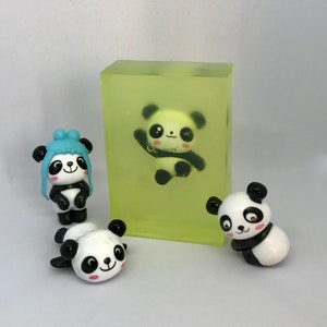 May include: Four small panda figurines, one is inside a clear green soap bar, the other three are on a white surface. The panda inside the soap bar is white with black markings and has a light blue bow tie. The other three pandas are black and white.