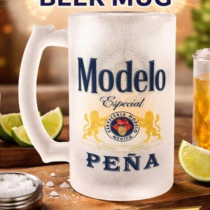 May include: Frosted beer mug with the Modelo Especial logo and the name "PEÑA" printed on it. The mug has a large handle and is surrounded by lime wedges and a small dish of salt. Text at the top says "Personalized BEER MUG".