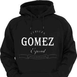 Op de afbeelding: Zwart hoodie met een wit grafisch ontwerp met de tekst "Cerveza Gomez Especial 1925" met een banner.