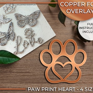 Op de afbeelding: Koperfolie overlay voor knutselen, met een pootprint met een hart erin. Het ontwerp is verkrijgbaar in vier maten. De afbeelding toont een gesoldeerd voorbeeld van het ontwerp.