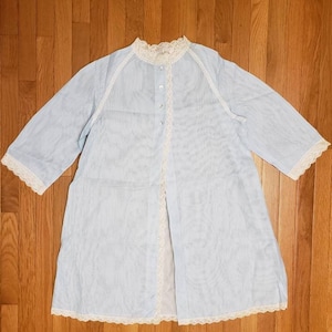 May include: A light blue sheer robe with white lace trim around the neckline, sleeves, and hem. The robe has a button closure and a front slit.