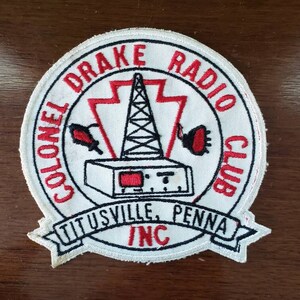 May include: White embroidered patch with red lettering that reads "Colonel Drake Radio Club, Titusville, Penna. Inc."  The patch features a red and black oil derrick with a red and black radio antenna.