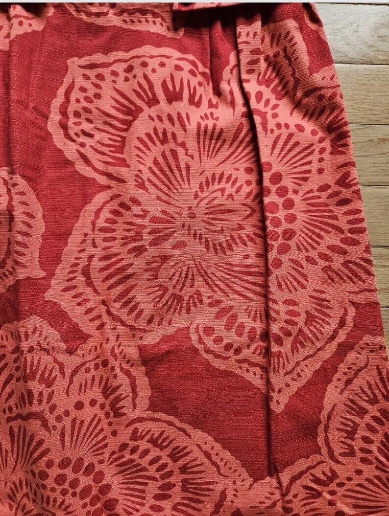 May include: Red fabric with a floral pattern. The fabric has a textured surface and a subtle sheen. The flowers are a lighter shade of red and have a detailed design.