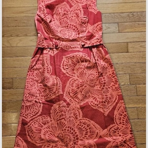 May include: A sleeveless red dress with a floral print. The dress has a fitted bodice and a full skirt. The dress is cinched at the waist with a belt.