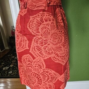 May include: A coral red dress with a floral print. The dress has a fitted bodice and a flared skirt. The floral print is a repeating pattern of large, stylized flowers.