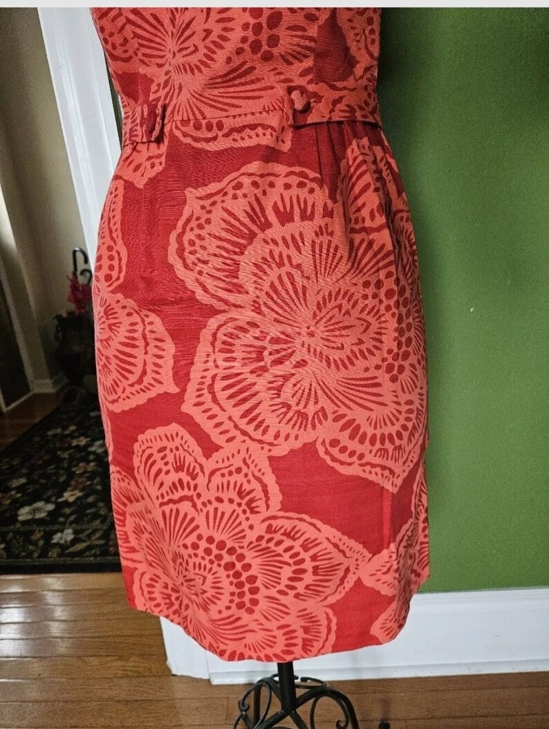 May include: A coral red dress with a floral print. The dress has a fitted bodice and a flared skirt. The floral print is a repeating pattern of large, stylized flowers.