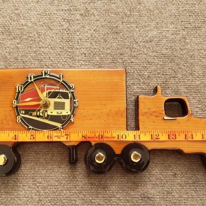 May include: Wooden wall clock shaped like a semi-truck with a clock face featuring a red and white semi-truck. The clock is 19 inches long.