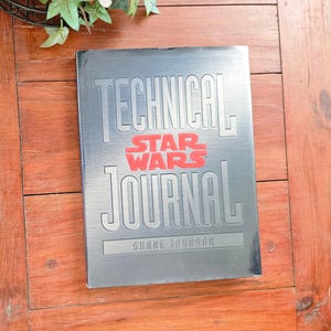Puede incluir: Un libro plateado con el título "Technical Star Wars Journal" y el nombre del autor "Shane Johnson" impreso en la portada.