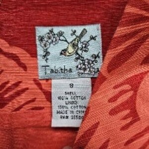 May include: A red and orange cotton dress with a floral print. The dress has a bird and flower design on the label. The label also says "Tabitha" and "8".