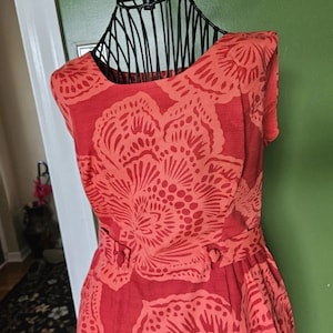 May include: A sleeveless red dress with a floral print. The dress has a round neckline and a fitted bodice. The skirt is full and flows out from the waist.