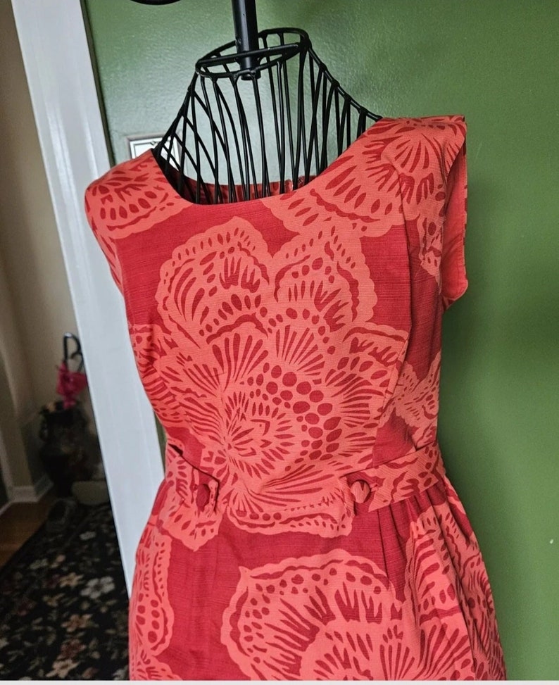 May include: A sleeveless red dress with a floral print. The dress has a round neckline and a fitted bodice. The skirt is full and flows out from the waist.