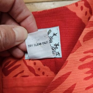 May include: Close-up of a red and white fabric with a floral pattern. A white tag with the text "Dry Clean Only" is attached to the fabric.