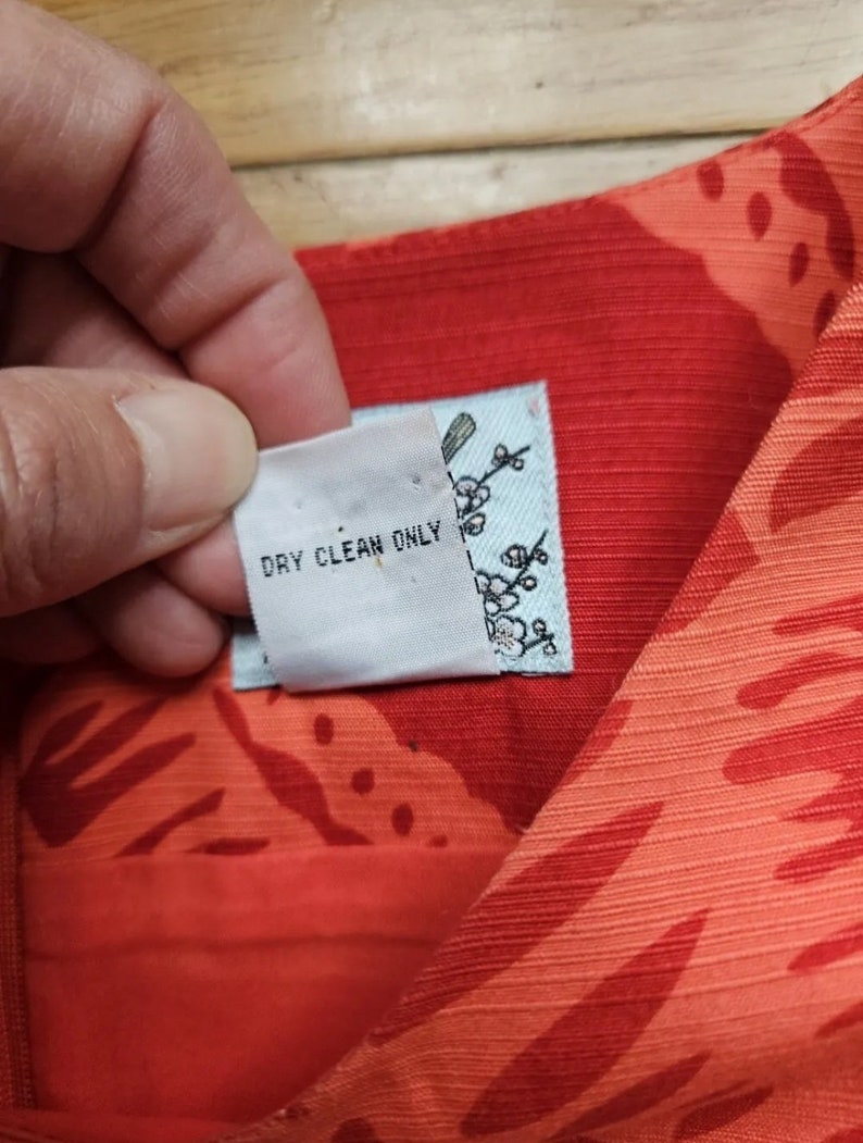 May include: Close-up of a red and white fabric with a floral pattern. A white tag with the text "Dry Clean Only" is attached to the fabric.