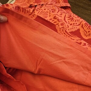 May include: Close-up of the inside of a red and orange floral print dress. The fabric is a soft, lightweight material.