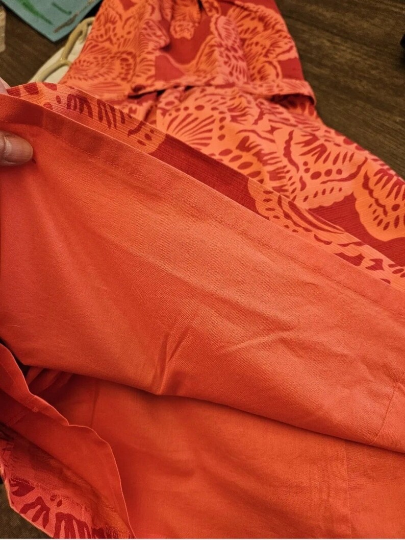 May include: Close-up of the inside of a red and orange floral print dress. The fabric is a soft, lightweight material.
