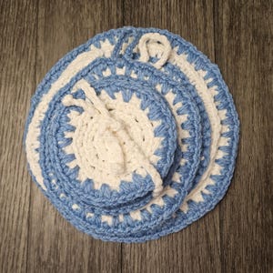 May include: Set of three crocheted pot holders in blue and white. The pot holders are layered on top of each other, with the smallest one in the center.