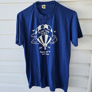 May include: A navy blue t-shirt with a white graphic of a hot air balloon, clouds, and text that reads "Up and Coming 20 Years" and "1963-1983 Keystone Tall Tree Girl Scouts."