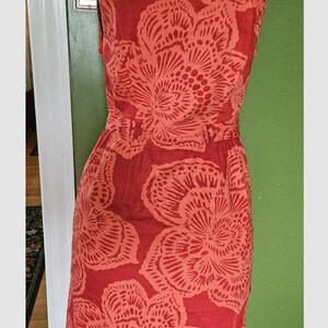 May include: A sleeveless coral dress with a floral print. The dress has a fitted bodice and a flowy skirt.