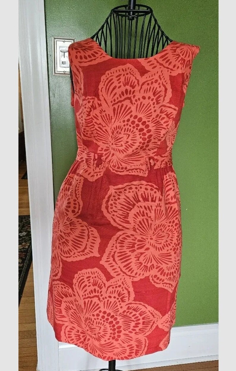 May include: A sleeveless coral dress with a floral print. The dress has a fitted bodice and a flowy skirt.