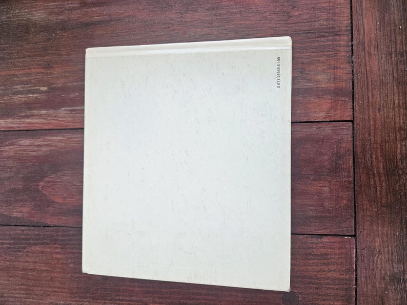 Op de afbeelding: Een boek met een lichtcr&egrave;mekleurige kaft, tegen een donkere houtnerf achtergrond. De kaft van het boek is effen, met een licht getextureerd oppervlak. De rug is zichtbaar en een reeks cijfers is aan de rechterkant gedrukt.