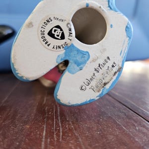 May include: A white ceramic figurine of a cartoon character with blue paint on the bottom. The bottom of the figurine has the text "&copy; WALT DISNEY PRODUCTIONS JAPAN" and a Disney logo.