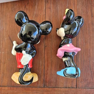 May include: A black and white ceramic figurine of Mickey Mouse wearing red shorts and black shoes.  A black and white ceramic figurine of Minnie Mouse wearing a pink dress and blue shoes.